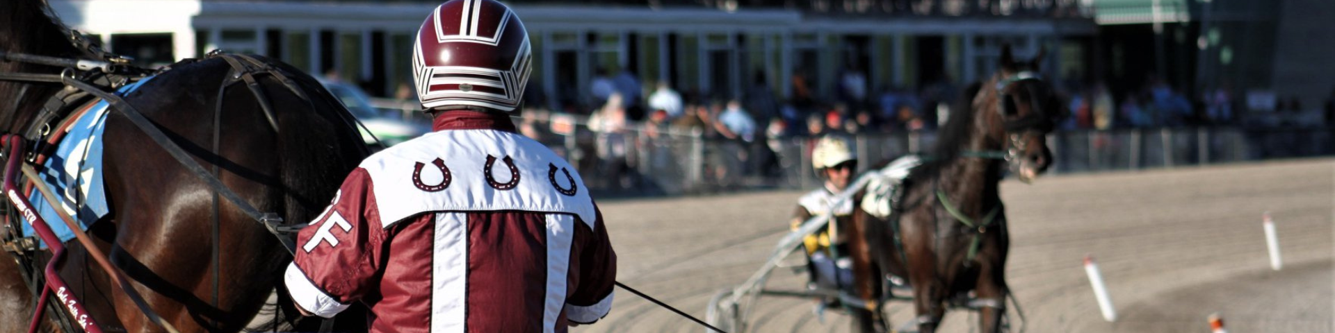 Photo of a jockey with a white and maroon jacket on a brown horse and a jockey in a yellow jacket on a brown horse on a race track