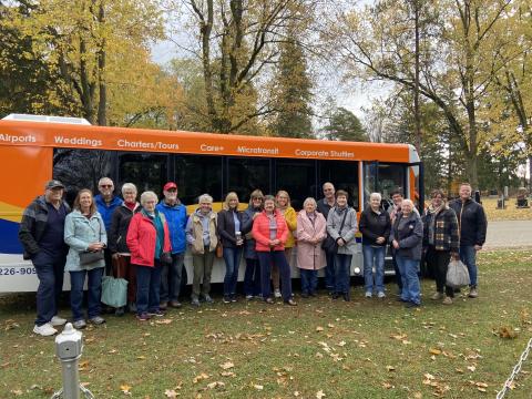 A group of people on a cloudy day standing in front of an orange travel bus