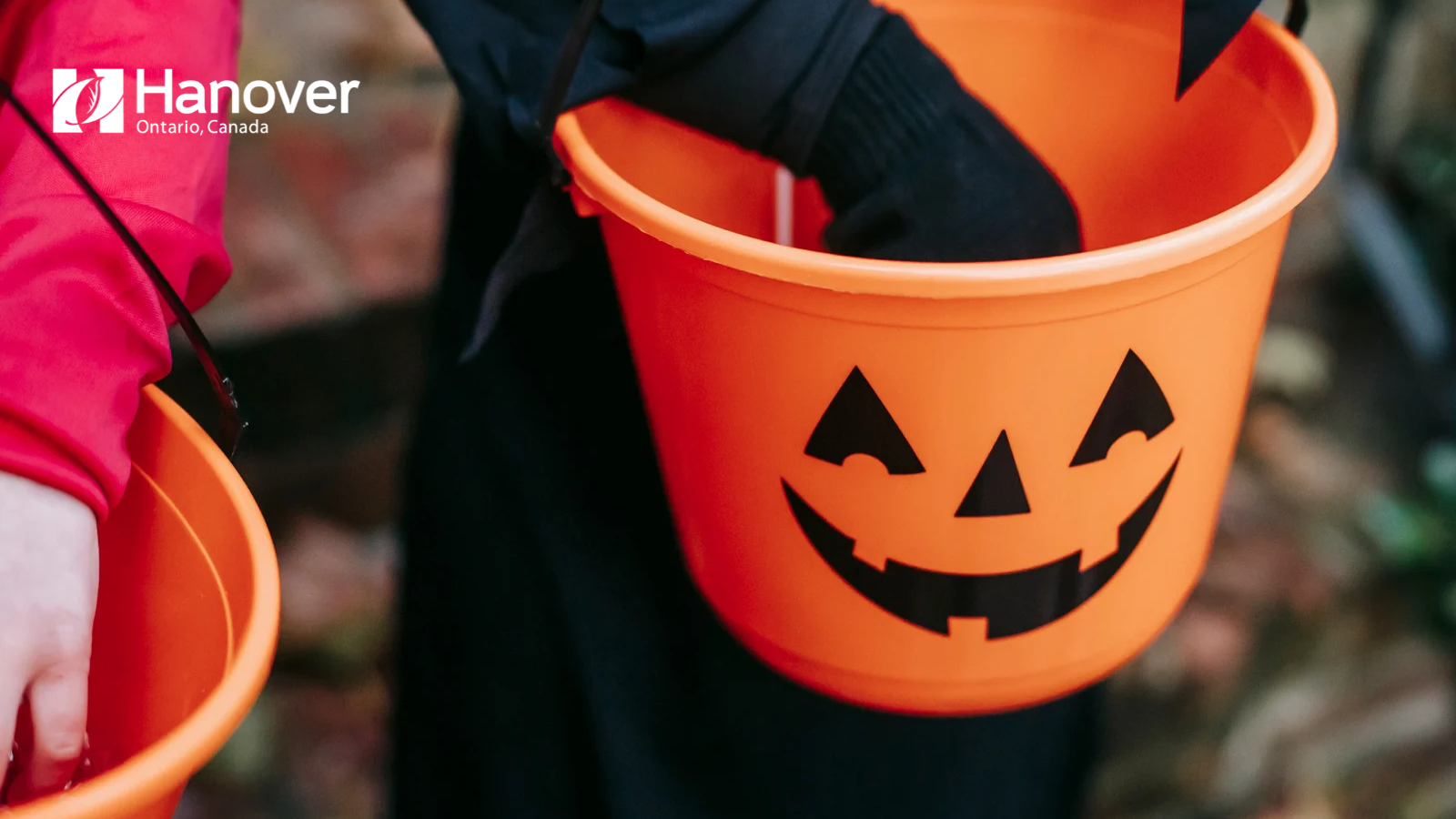 Child holding a trick or treat bucket in a black costume with white town of hanover logo to left